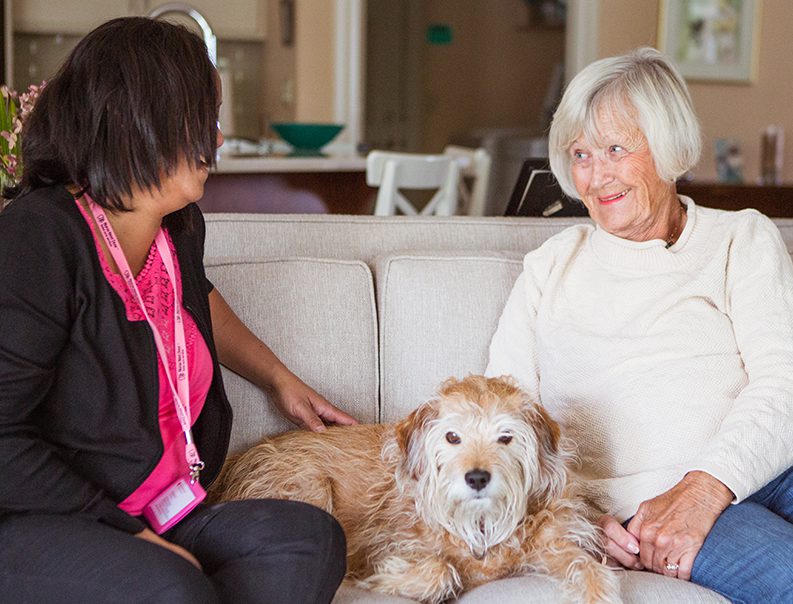 nurse care giver sitting with an elderly woman and her dog after doing house keeping helping to keep her living in her own home