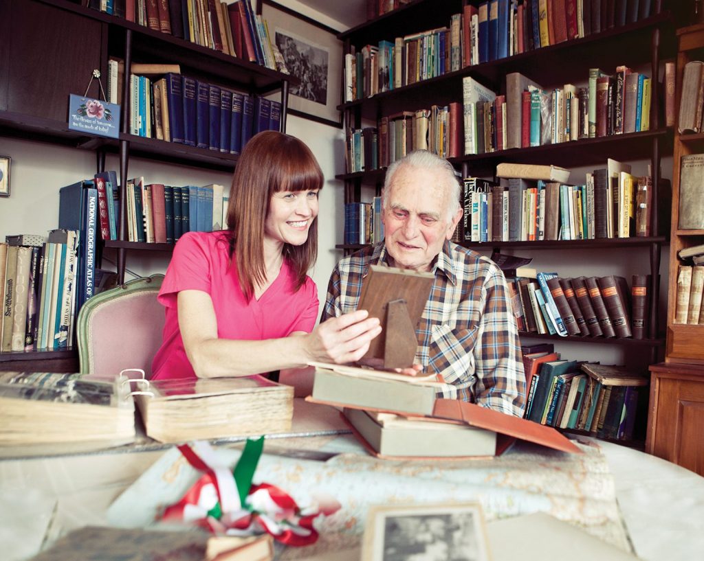 Care giving nurse helping an elderly man with Sundowners to look at photographs and reminisce which will help his symptoms