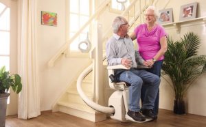 elderly couple using a chair lift on their stairs to assist them to stay at home