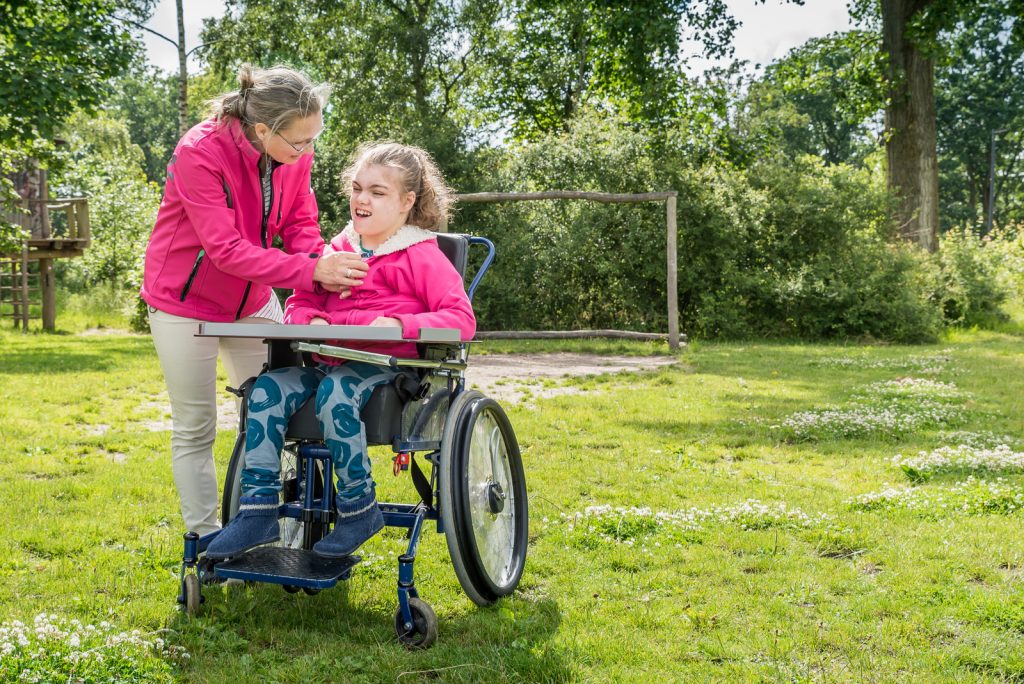 A young girl with a disability who is being helped by a caregiver