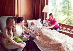 Palliative Care Patient in bed surrounded by family and nurse