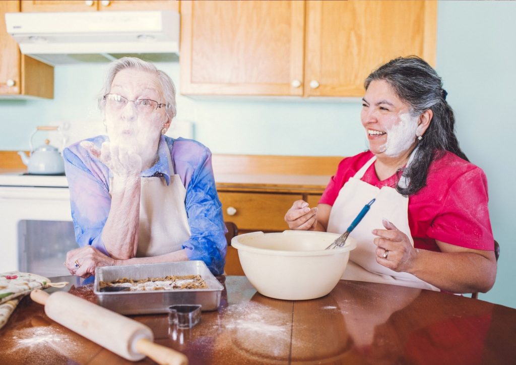 Elderly woman having fun in her kitchen with Nurse Next Door carergiver