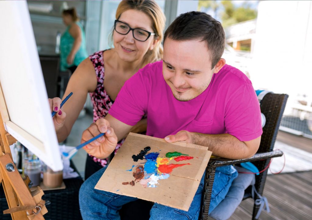 Young man with Down Syndrome painting with carer